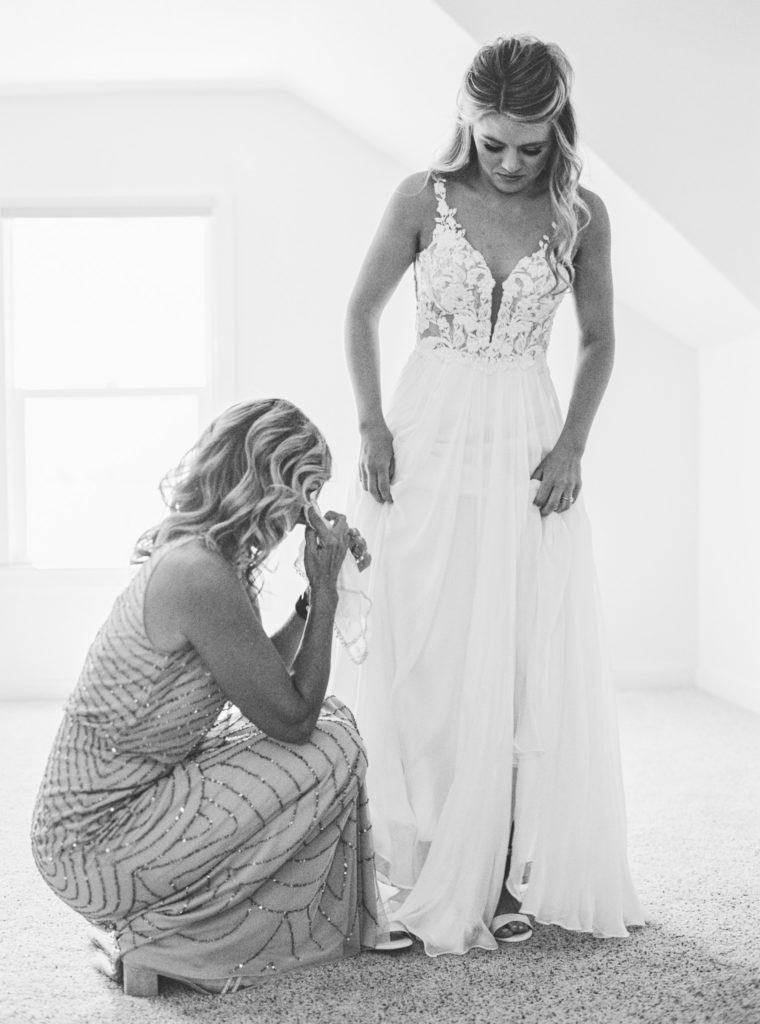Mother of the bride wipes away a tear of joy as she helps her daughter into her wedding dress.